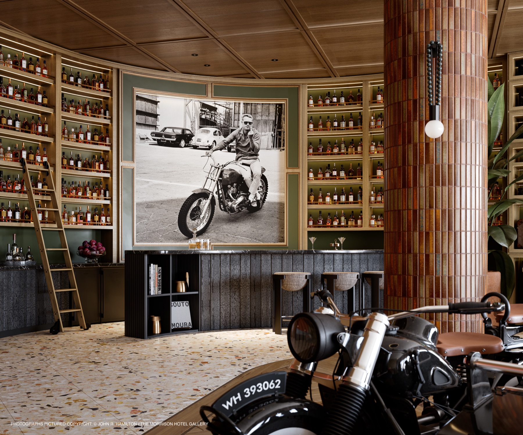 The bourbon bar at The Rider Residences Wynwood — curved terrazzo floors, floor-to-ceiling whiskey shelves with a library ladder, warm tiled columns, vintage motorcycles, and a towering black-and-white portrait, a study in mid-century elegance and Americana soul.